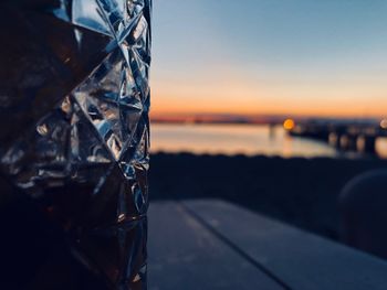 Close-up of glass on table against sea during sunset