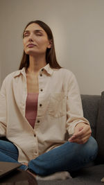 Beautiful young woman sitting against wall at home