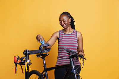 Portrait of young woman riding bicycle against yellow background