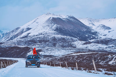 Man sitting on car roof against snowcapped mountains