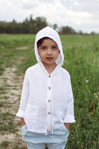 Boy child in a green field in summer in a white shirt with a hood made  linen in shorts and sandals