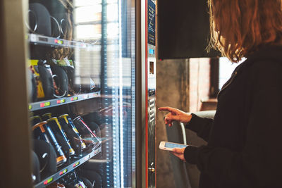 Woman paying for product at vending machine using contactless method of payment with mobile phone