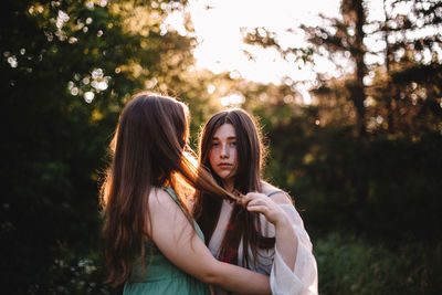 Young lesbian couple romancing while standing in forest during summer