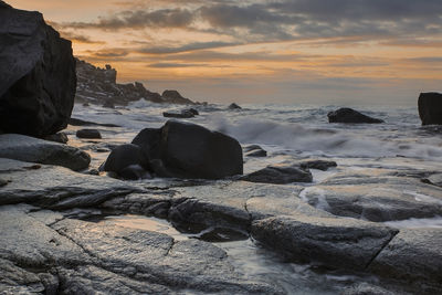 Rocks on beach against sky during sunset