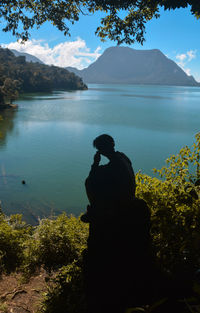 Side view of silhouette man looking at lake by mountain