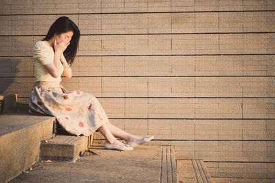 Sad woman sitting on steps against wall