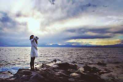 Rear view of man standing on beach against cloudy sky