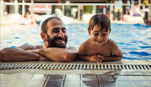 Smiling shirtless father with son relaxing at poolside