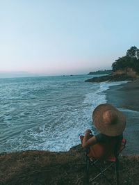 Rear view of man sitting at beach against sky