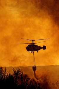 Silhouette helicopter against orange sky