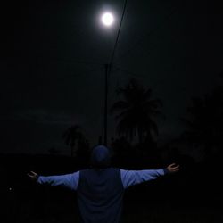 Rear view of man with arms raised standing at night