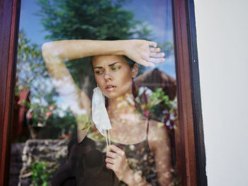 Portrait of young woman looking through window