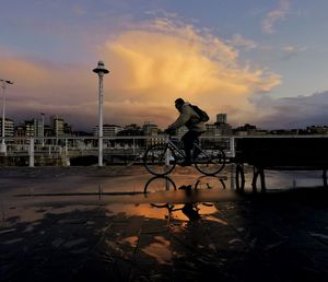 Man riding bicycle on street against sky during sunset