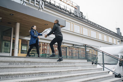 Low angle view of messenger delivering box to female customer in city