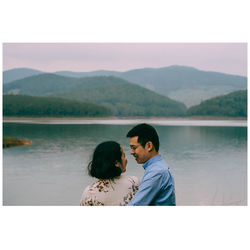 Couple kissing on lake by mountains against sky