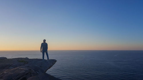 Man standing on cliff by sea against sky