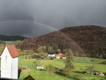 Scenic view of rainbow over field by houses against sky