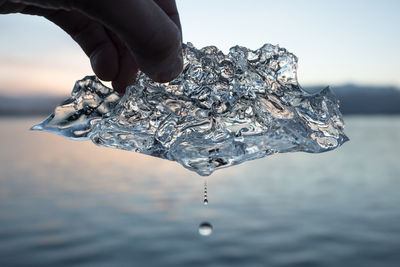 Close-up of hand holding ice against sea