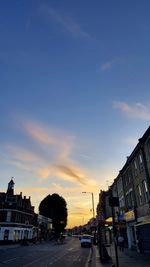 Cars on city street against sky during sunset