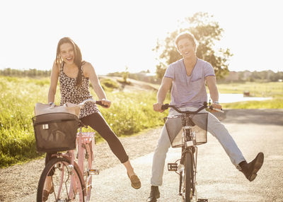 Portrait of happy young couple with legs apart cycling on country road