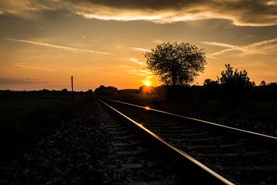 Railroad tracks amidst trees against sky during sunset