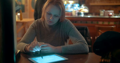 Young woman using phone while sitting on table