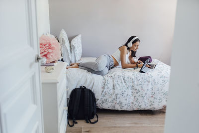 Girl with headphones lying on bed using wireless technologies at home