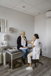 Doctor consulting senior patient siting on bed in clinic