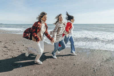 Carefree friends running at beach on sunny day