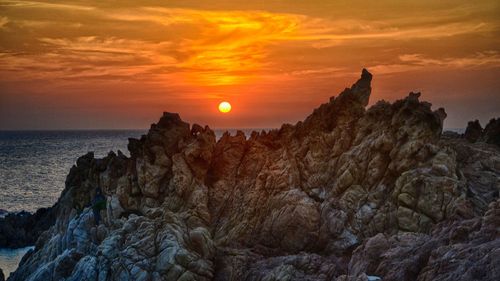 Rock formations at sea against cloudy sky during sunset