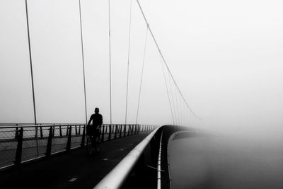 Man bicycling on bridge against clear sky