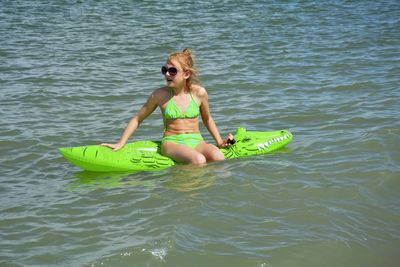 Girl wearing bikini sitting on inflatable crocodile in lake