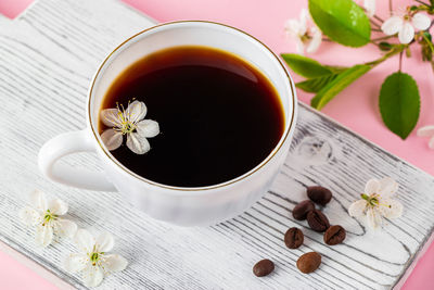 Cup of strong espresso coffee and delicate spring flowers on pink background. springtime 