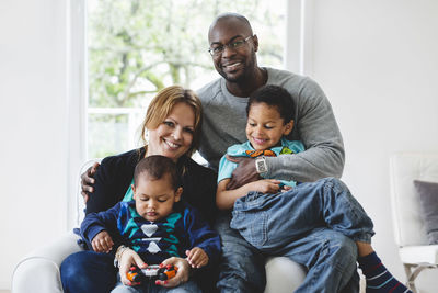 Portrait of happy multi-ethnic parents sitting with children at home