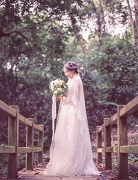 Side view of bride with bouquet standing on footbridge