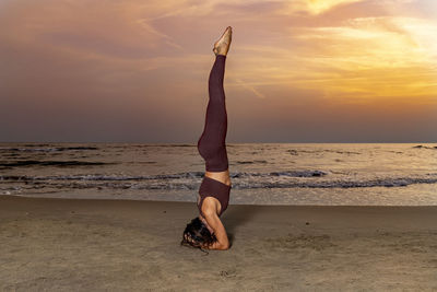 Woman practicing yoga on the beach at sunset. woman in sirsana position on the sand. 