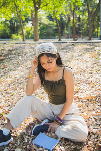 An asian woman in green singlet,  sitting on ground over dry leaves