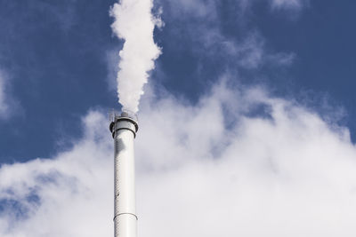 Low angle view of smoke stack emitting pollution in sky