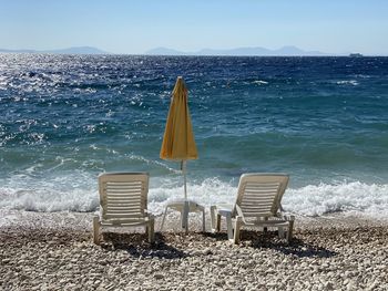 Empty chairs on beach against sky