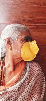 Close-up of senior woman wearing flu mask standing by wooden wall