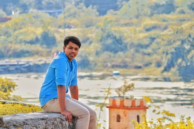 Portrait of young man sitting on rock by sea