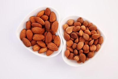 Close-up of almonds in heart shape bowls over white background