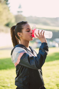 Side view of woman drinking water while standing on field