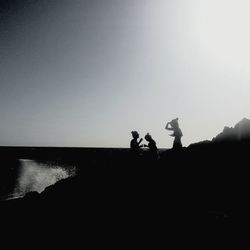 Silhouette people on sea against clear sky