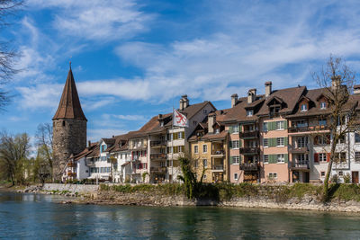 Buildings at waterfront against cloudy sky