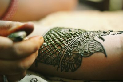 Artist drawing henna tattoo on cropped hand of bride
