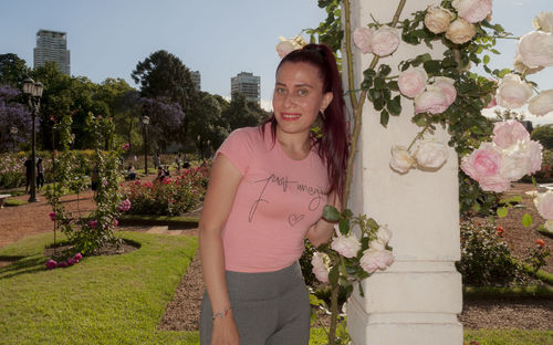 Portrait of smiling young woman standing by flowering plants