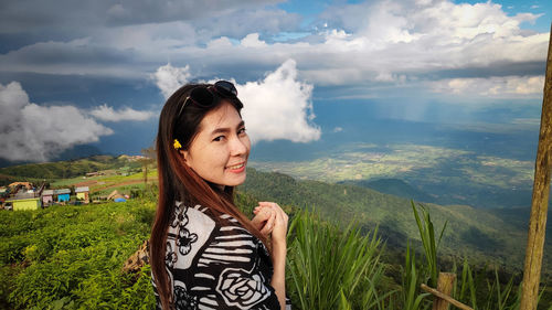 Portrait of young woman standing on mountain against cloudy sky