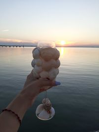 Hand holding sea against sky during sunset