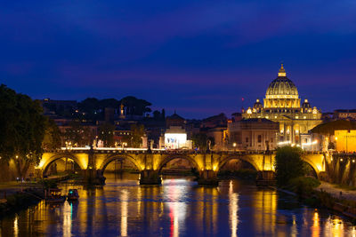 Illuminated bridge over river against buildings at dusk